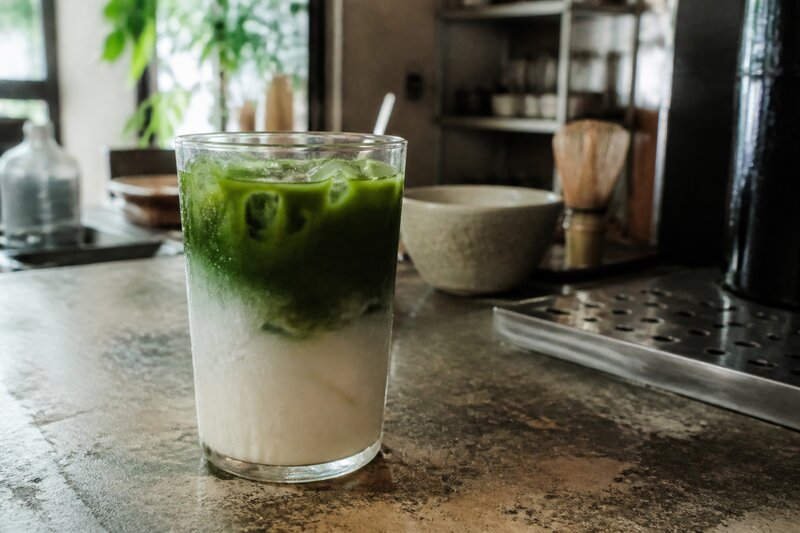 A layered iced matcha latte in a clear glass with vivid green matcha poured over milk